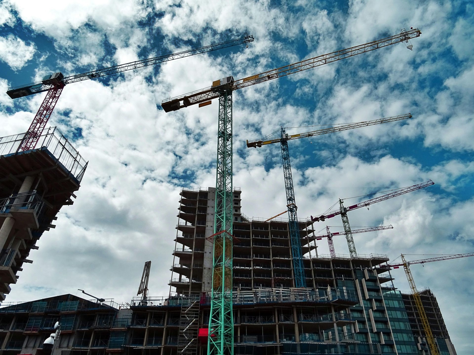 Chantier de construction urbain avec de nombreuses grues encadrant des gratte-ciels en plein essor sur un ciel bleu.
